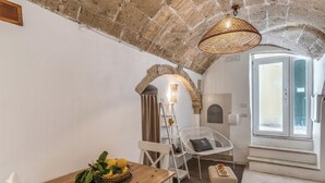 A cozy room with a wooden table, white chairs, a wicker chair, a small stool, a basket of lemons, and a hanging light fixture. - La Cummare - Le Case di Valentina (Gallipoli)