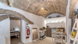 A compact kitchen with a stone ceiling, a dining area with a table and chairs, and a small seating area with a yellow vase. - La Cummare - Le Case di Valentina (Gallipoli)