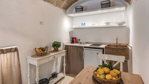 A compact kitchen with a brick archway, a white countertop, a small refrigerator, and a wooden dining table with a basket of lemons. - La Cummare - Le Case di Valentina (Gallipoli)