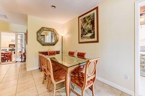 A dining area with a glass-top table, wooden chairs, a large mirror, and a framed painting on the wall. - Anastasia Lodge (St Augustine Beach)