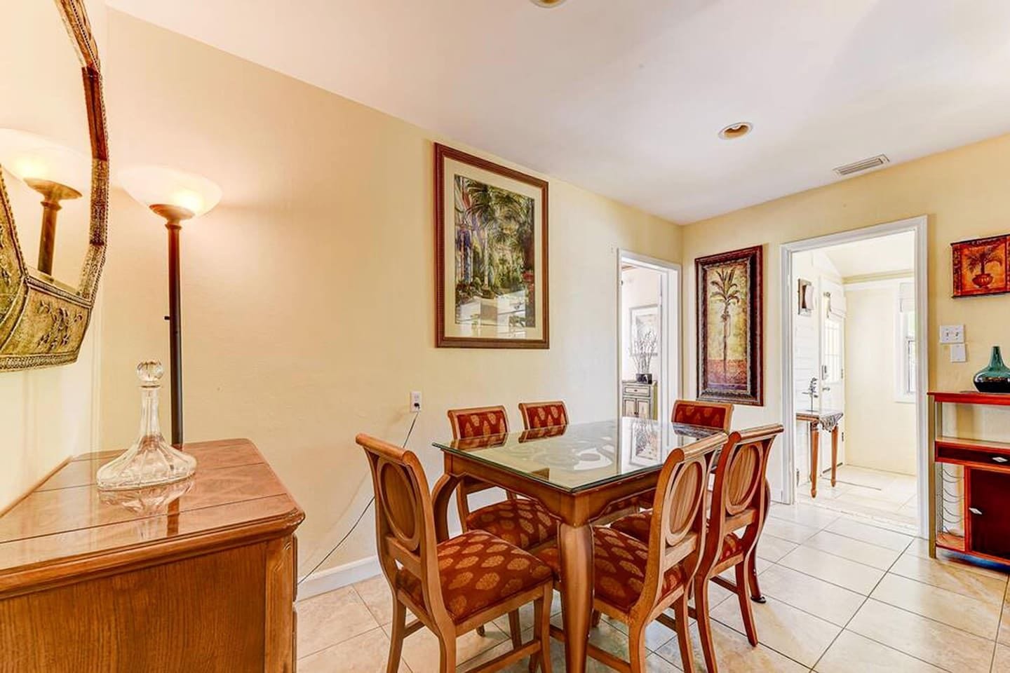 Uma área de refeições com mesa de vidro, cadeiras de madeira e um candelabro.