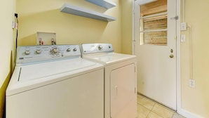 A laundry room with two washing machines, a door with a wooden panel, and a shelf above the machines. - Anastasia Lodge (St Augustine Beach)