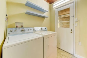 A laundry room with two washing machines, a door with a wooden panel, and a shelf above the machines. - Anastasia Lodge (St Augustine Beach)
