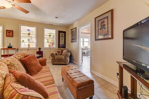 A living room with a sofa, ottoman, armchair, and a television on a stand. - Anastasia Lodge (St Augustine Beach)