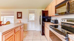 A kitchen with wooden cabinets, a refrigerator, a microwave, and a stove. - Anastasia Lodge (St Augustine Beach)