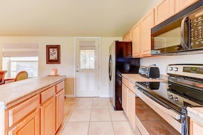 A kitchen with wooden cabinets, a refrigerator, a microwave, and a stove. - Anastasia Lodge (St Augustine Beach)