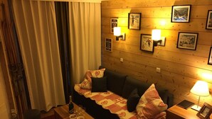 Une pièce chaleureuse avec un mur en bois, un canapé agrémenté de coussins à motifs, une petite table avec une bouteille et des verres, et des tableaux encadrés accrochés au mur.