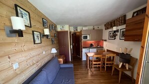 Un espace de vie compact doté d’un mur en bois, d’un canapé bleu, d’un coin repas avec une table et des chaises, et d’une kitchenette équipée d’un four à micro-ondes.
