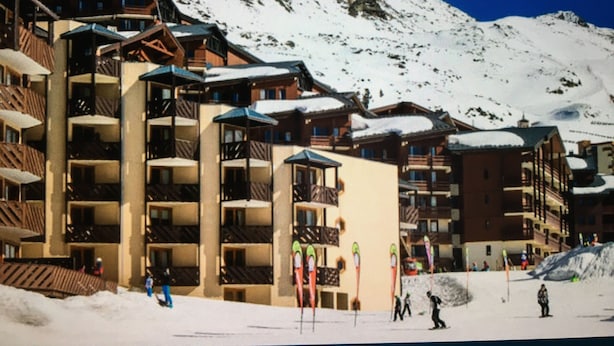 Un hôtel à plusieurs étages, doté de balcons, avec des pistes de ski en arrière-plan.