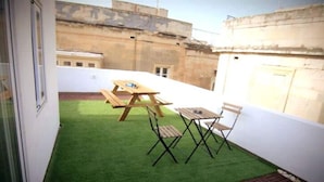 A small patio with artificial grass, a wooden table, and two chairs. - Citta Cospicua Suites - Polverista Suite (Bormla)