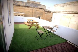 A small patio with artificial grass, a wooden table, and two chairs.