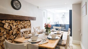 A dining area with a wooden table set for four, a clock on the wall, and a kitchen in the background. - Field View - sleeps 5 guests  in 3 bedrooms (Tarlton)