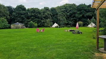Un espace extérieur verdoyant avec des tables de pique-nique, une structure en bois et une tente en arrière-plan.