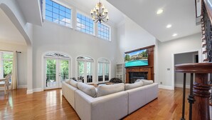 A spacious living room with a large sectional sofa, wooden flooring, a fireplace, and a TV mounted on the wall. - Norris Lake Manor-Exquisite Waterfront with *Private Dock *Pool *Hot tub *Game room  (Caryville)