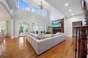 Relax in this spacious living area with a high ceiling and large windows, featuring a comfortable sofa and flat-screen TV.