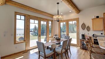 A spacious dining area with a wooden table and chairs, large windows offering a view of the outdoors, and a kitchen area with wooden cabinets and a countertop.