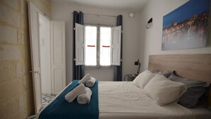 Una habitación de hotel con una cama, una ventana con cortinas, un cuadro en la pared y una puerta.