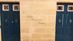 Fachada de edificio con dos puertas azules, cada una con una reja metálica decorativa y un tirador de bronce. El número "27" es visible en la pared entre las puertas.