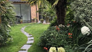Un jardin avec un chemin de pierres menant à un bâtiment doté d’une porte en verre.