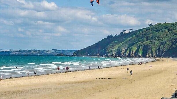 Une plage avec un ciel dégagé, un cerf-volant qui vole et des gens qui se promènent le long du rivage.