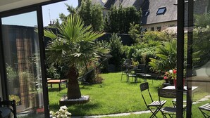 Une chambre moderne dotée de grandes portes vitrées donnant sur un jardin. On y trouve deux petites tables rondes et quelques chaises.
