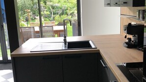 Une cuisine moderne dotée d’un grand îlot central, de meubles de couleur noire et offrant une vue sur un jardin grâce à une porte-fenêtre coulissante.