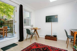 A room with a sliding glass door, a round table with chairs, a flat-screen TV mounted on the wall, and a small wooden cabinet. - Stunning 1BDR Basement Flat with Garden in Camden (London)