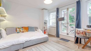 A modern bedroom with a bed, a desk, a chair, a TV, and a window with curtains. - Stunning 1BDR Basement Flat with Garden in Camden (London)