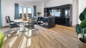 A modern kitchen with black cabinets, a central island, and a dining area with a table and chairs. - Admiralsdeck Panoramablick, Finnische Sauna, 3 Baeder, Fahrstuhl, 2 Terrassen (Olpenitz)