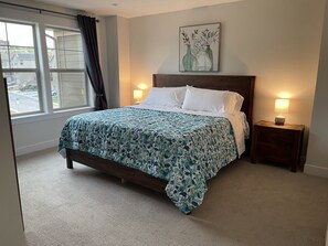 Un lit bien fait, recouvert d’une couvre-lit à motifs floraux, avec deux lampes de chevet, une table de nuit et une fenêtre avec des rideaux.