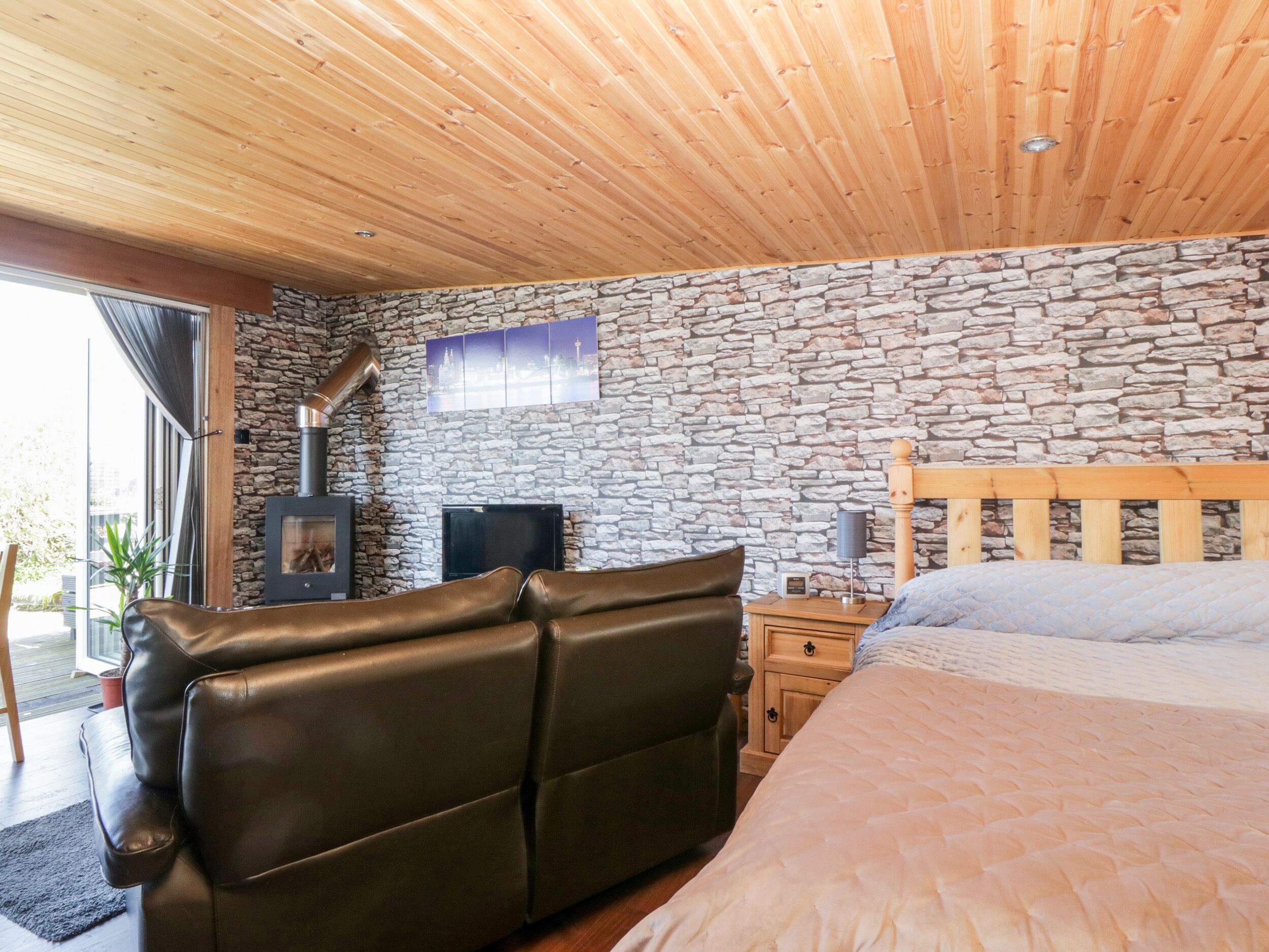 A bedroom with a stone wall, a bed, a sofa, a TV, and a fireplace.