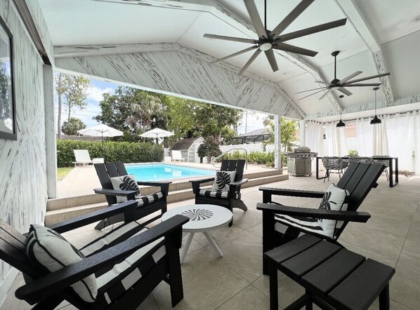 An outdoor patio area with a pool, black and white furniture, ceiling fans, and umbrellas.