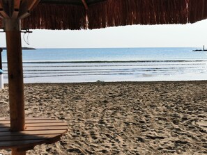 A beach with a thatched roof structure, sandy beach, and calm sea. - Studio apartment 50 m from the beach with A/C, Wi-Fi & parking (Montesilvano)