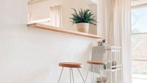 Quarto minimalista com paredes brancas, piso de concreto, teto de madeira, planta em vaso, prateleira branca com objetos e janela com cortinas.