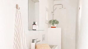 Casa de banho com toucador branco, toalha, espelho, chuveiro e luz de teto.