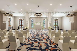 Un grand hall doté d’un tapis à motifs, de chaises blanches et d’appareils d’éclairage décoratifs.