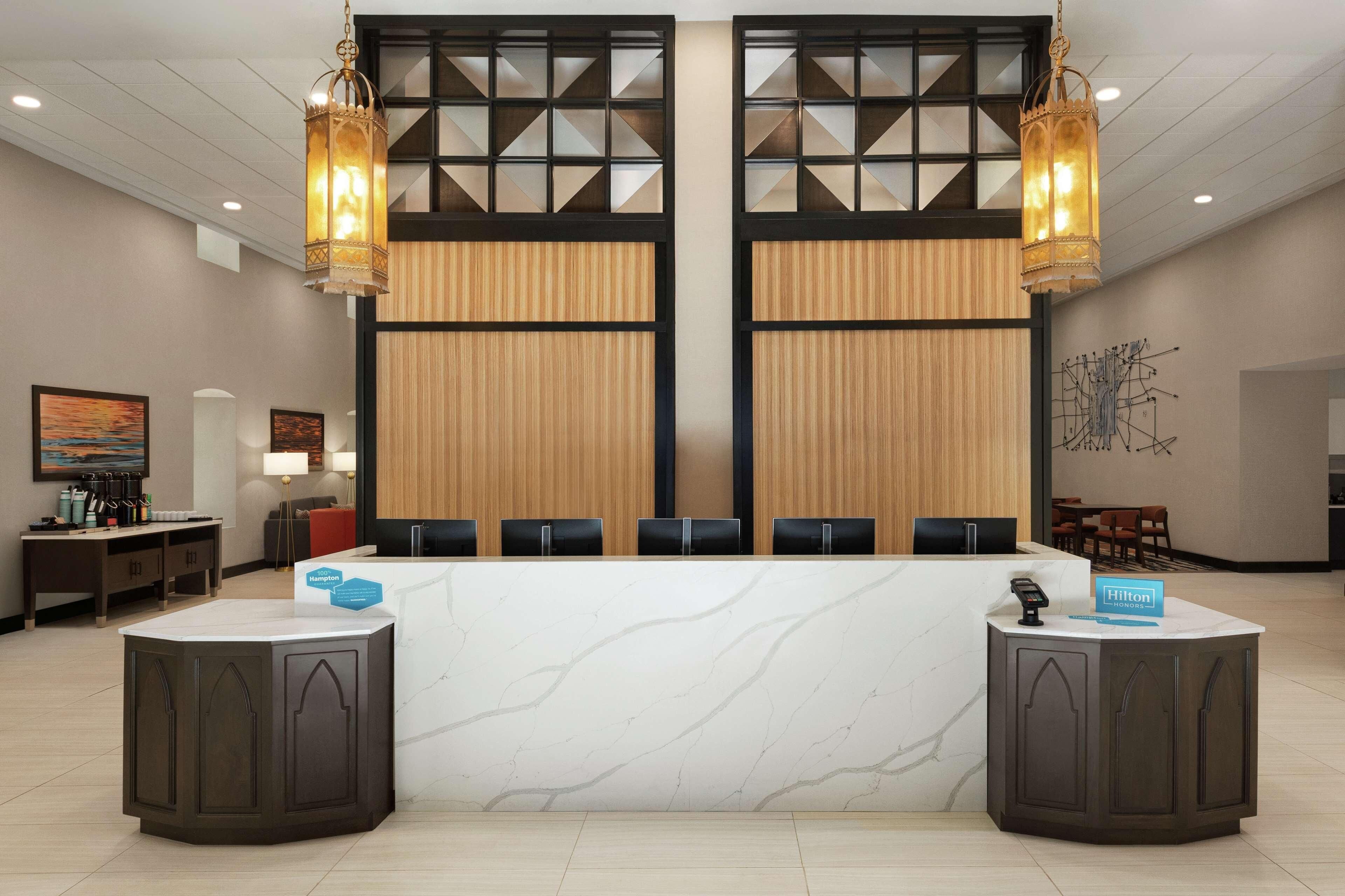 Ein Hotel-Empfangsbereich mit Marmor-Theke, zwei großen Hängeleuchtern und modernem Interieur.