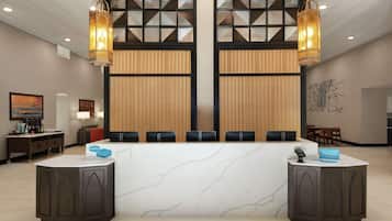 Ein Hotel-Empfangsbereich mit Marmor-Theke, zwei großen Hängeleuchtern und modernem Interieur.