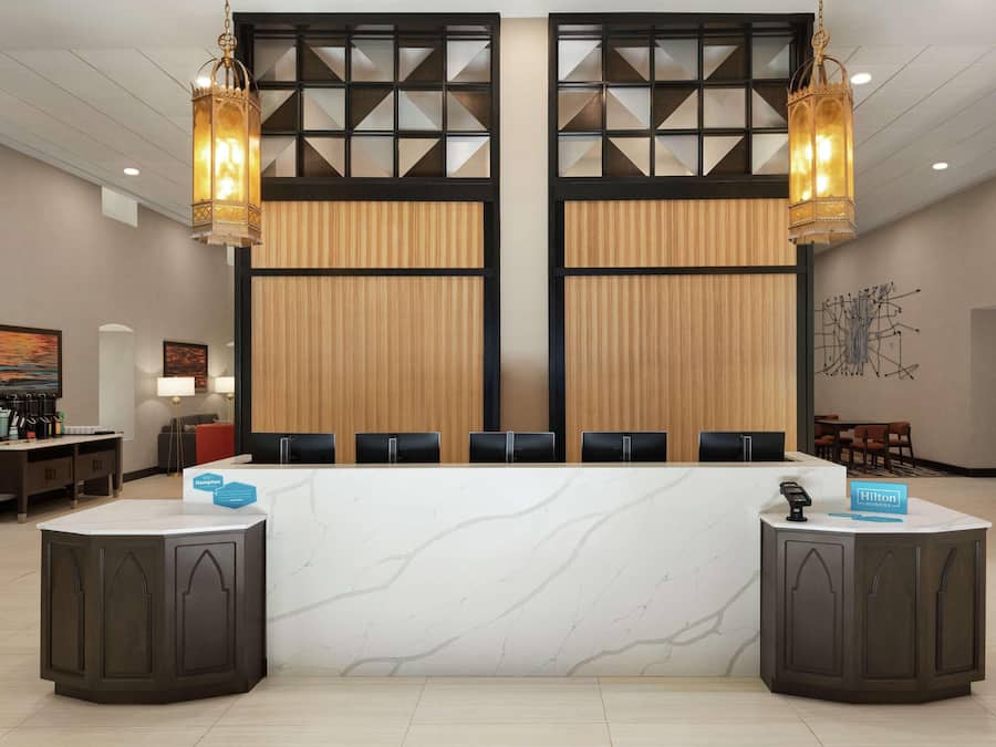 Zona de recepción de hotel con mostrador de mármol, dos grandes lámparas colgantes y un diseño de interiores moderno.