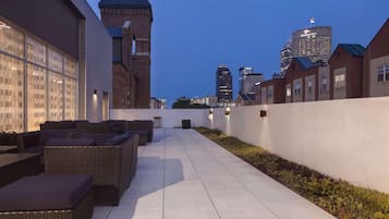 A rooftop patio with outdoor furniture, a city skyline in the background, and a brick building with a tower.