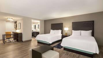 A hotel room with two beds, a desk, a chair, and a small table.