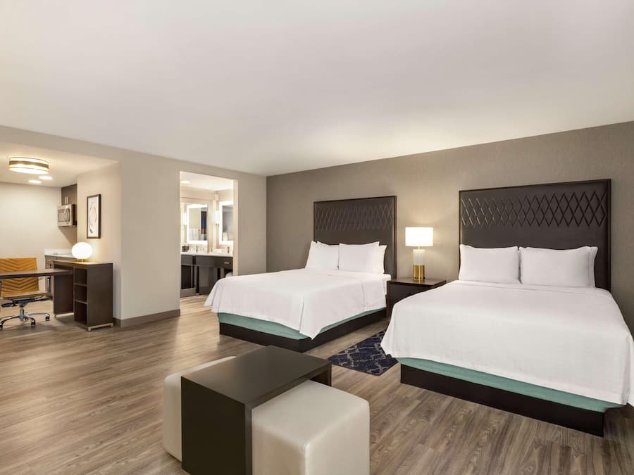 A hotel room with two beds, a desk, a chair, and a small table.