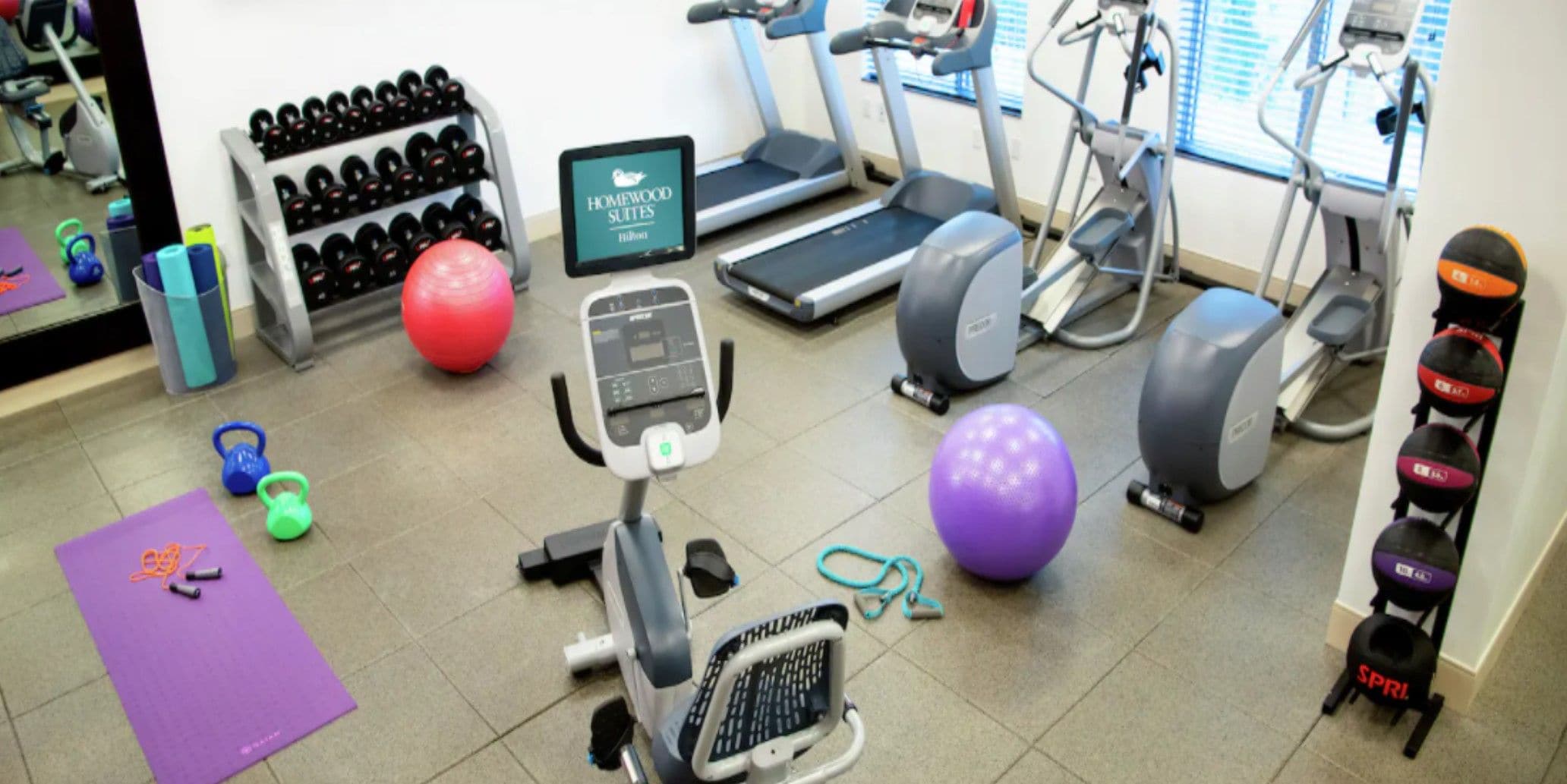 Une salle de sport équipée de tapis de course, de vélos elliptiques et de différents ballons d’exercice.