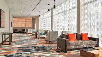 A hotel lobby with a patterned carpet, seating area with sofas and chairs, and large windows with sheer curtains.