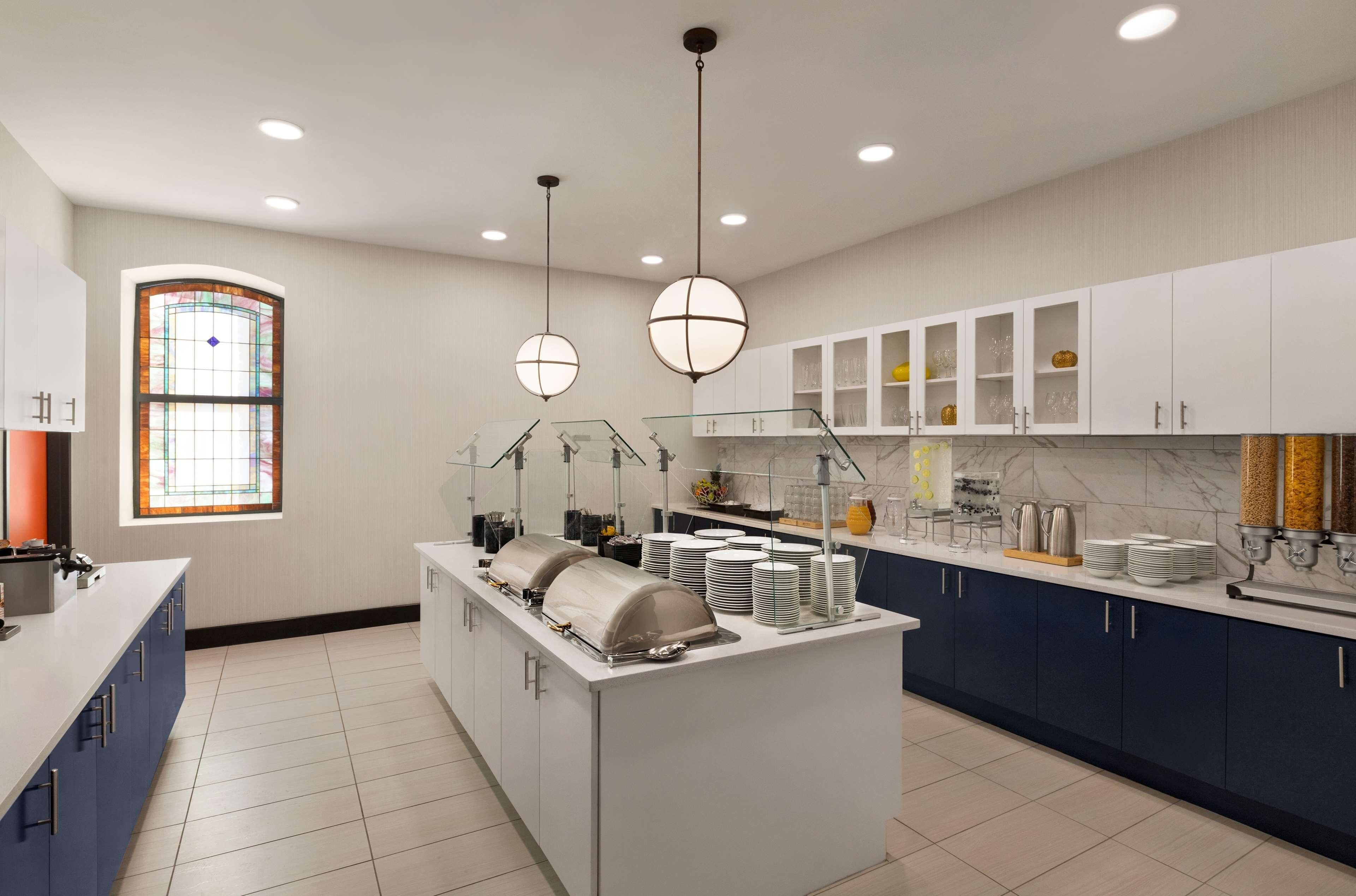 A modern kitchen with a central island, white cabinets, and a large window with stained glass.