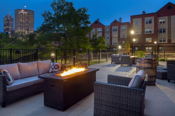 An outdoor patio with a fire feature, wicker furniture, and a view of a city skyline at dusk.