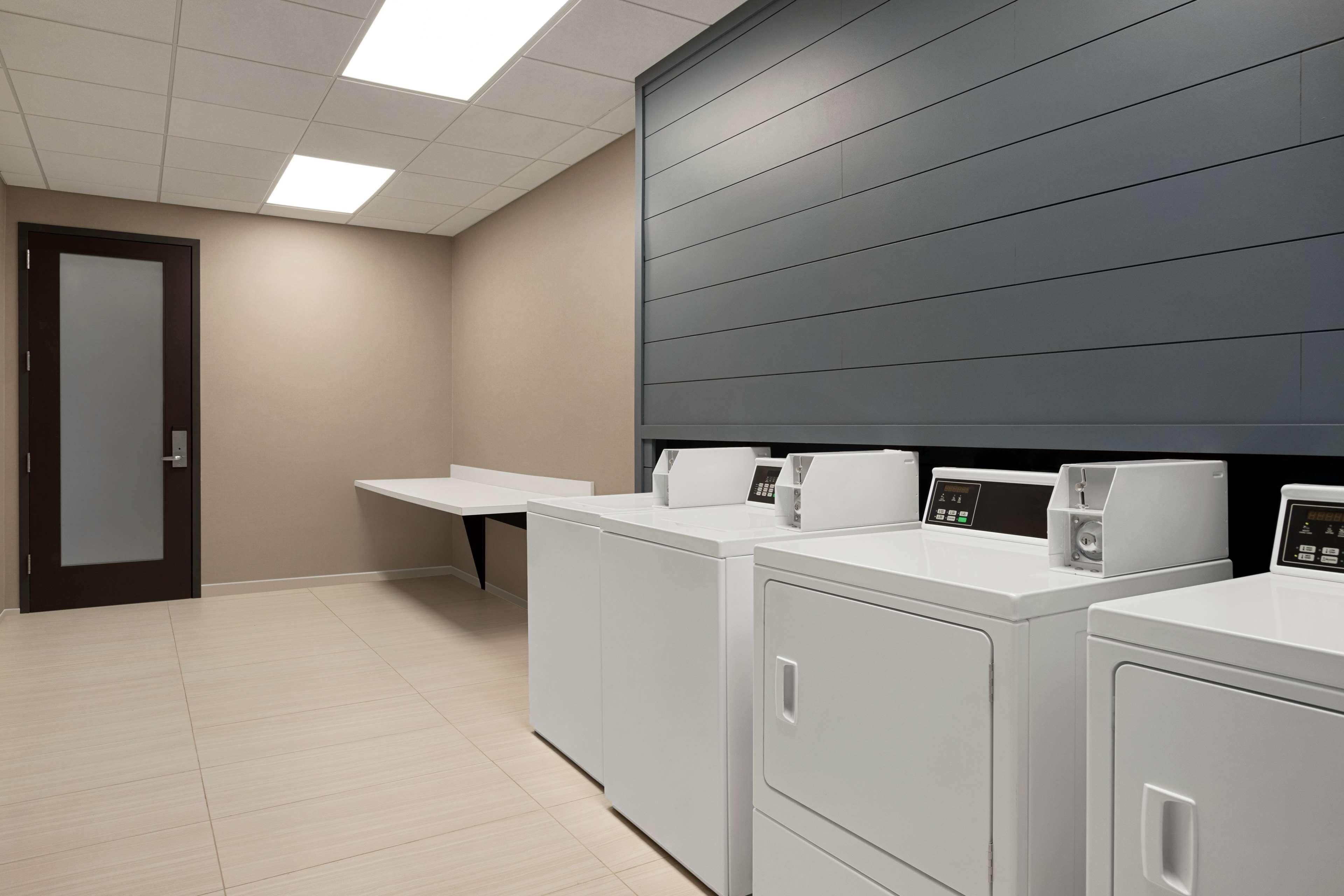 A laundry room with four white washers and dryers, a bench, and a door.