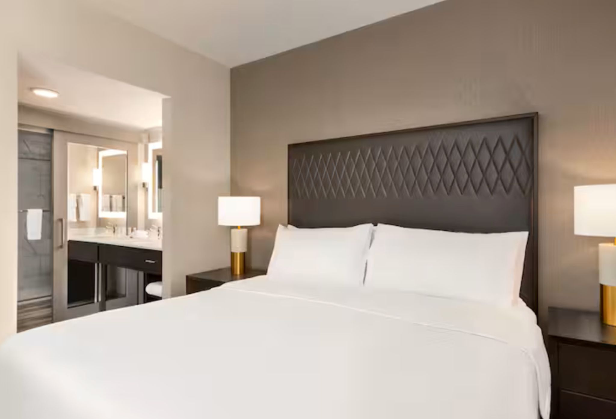 Una habitación de hotel con una cama grande, un escritorio con espejo y dos lámparas de noche.