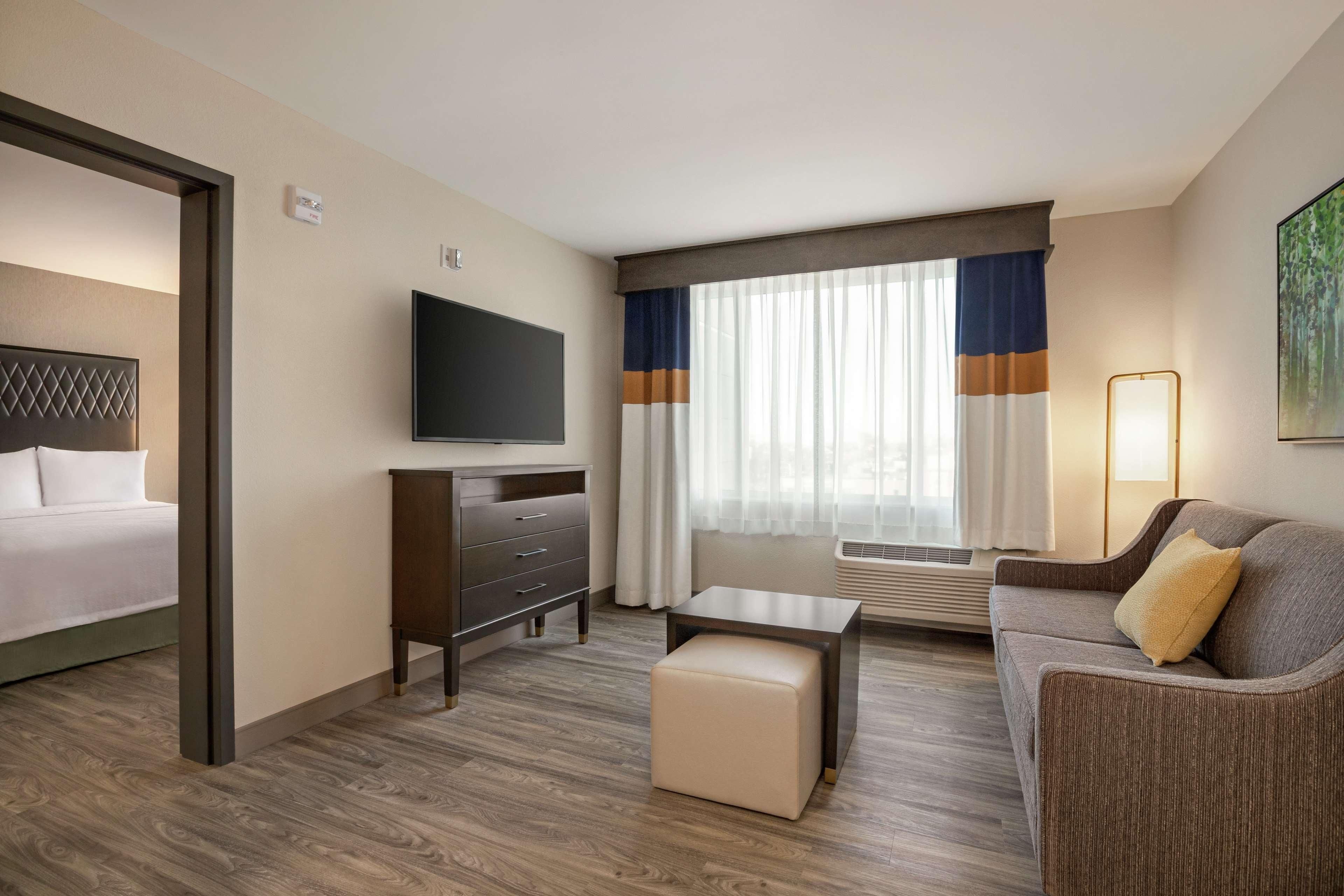 A hotel room with a bed, a TV, a desk, a sofa, and a window with curtains.