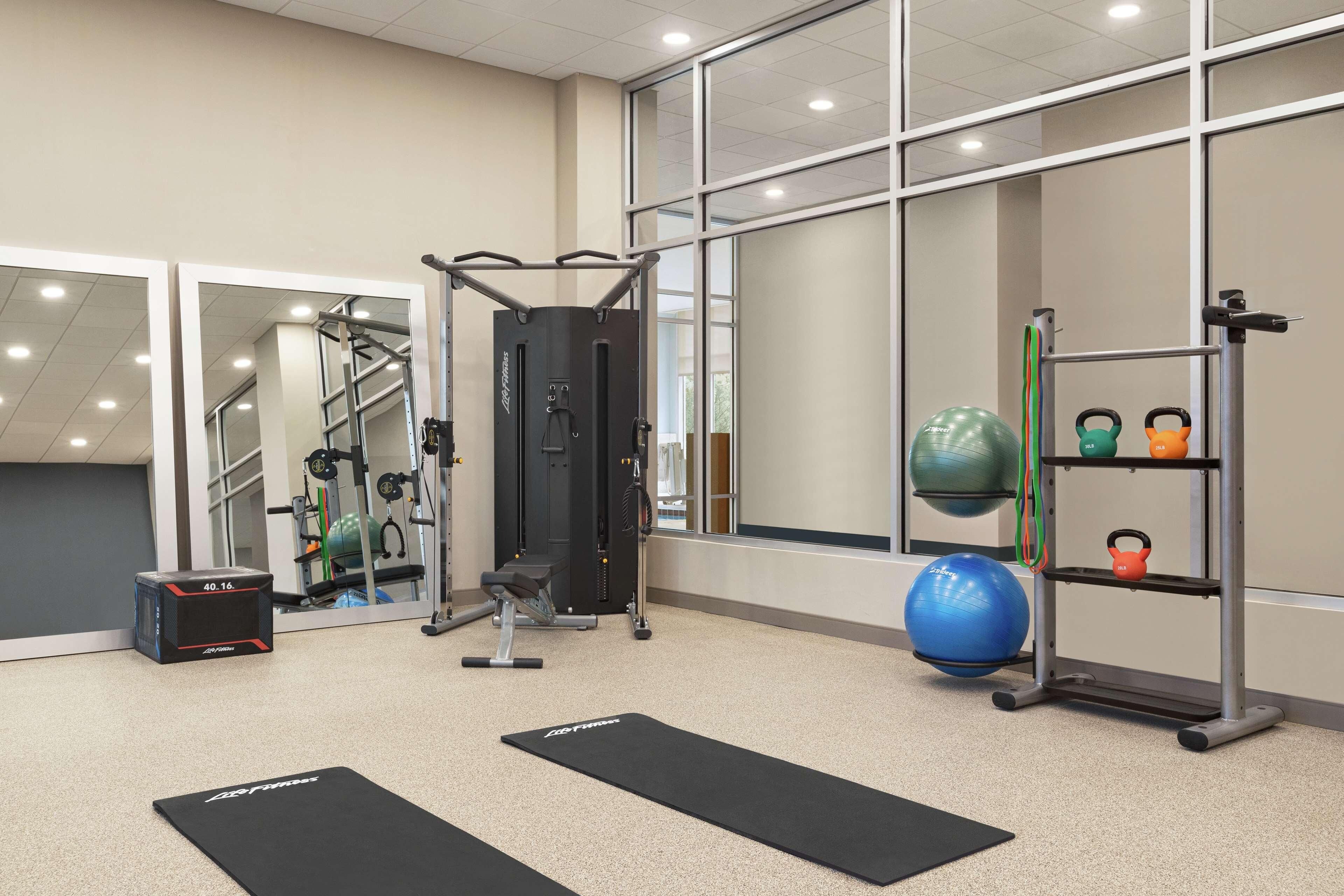 A gym with exercise equipment, black mats, and a kettlebell rack.